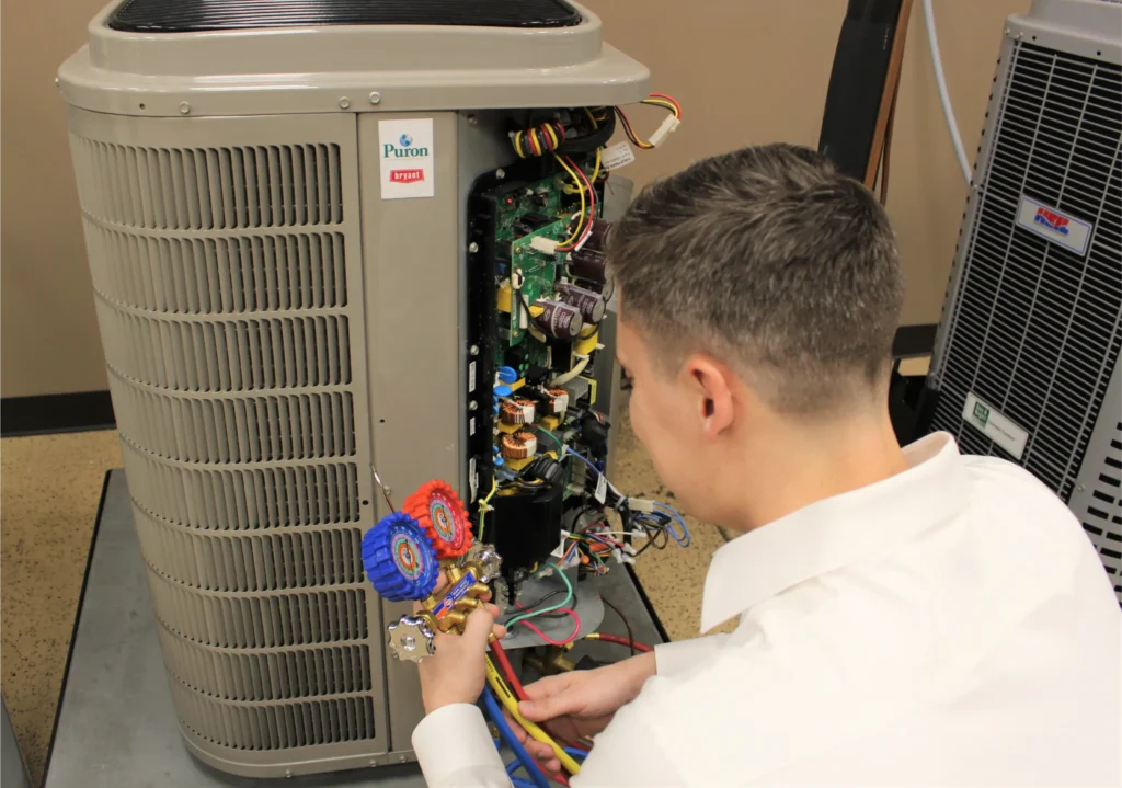 HVAC technician inspecting and servicing an outdoor air conditioning unit using a refrigerant pressure gauge manifold.